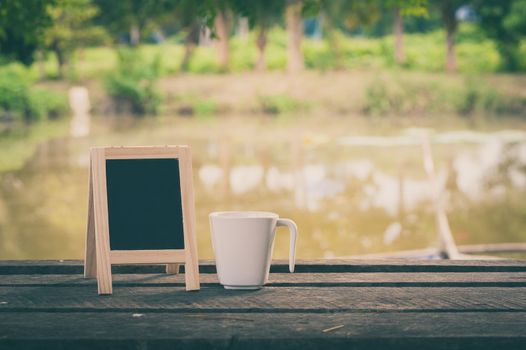 Small A-frame blackboard with blank area for text or message and coffee cup on rustic wood table in morning time with vintage filter effect