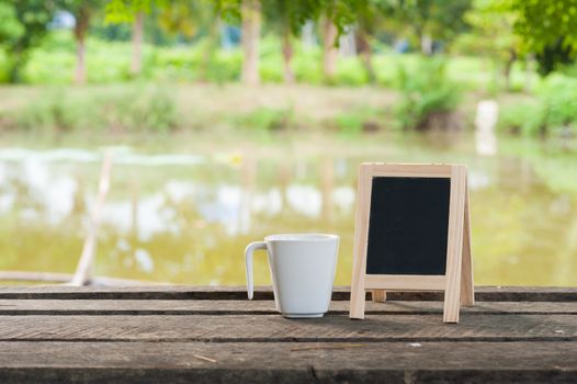 Small A-frame blackboard with blank area for text or message and coffee cup on rustic wood table in morning time