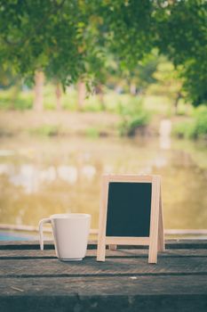 Small A-frame blackboard with blank area for text or message and coffee cup on rustic wood table in morning time with vintage filter effect
