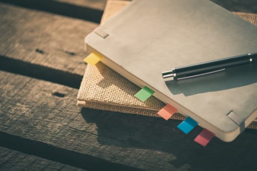 Pen and notebooks on rustic wood table at outdoor area with morning time on summer with vintage filter effect