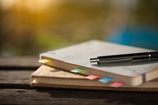 Pen and notebooks on rustic wood table at outdoor area with morning scene in summer time