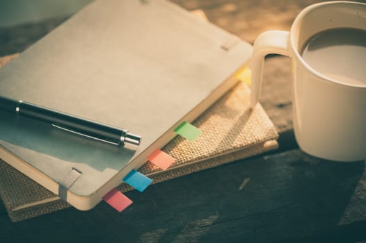 Pen, notebooks, and coffee cup on rustic wood table at outdoor area in morning time with vintage filter effect