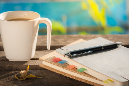 Pen, notebooks, and coffee cup on rustic wood table at outdoor area in morning time
