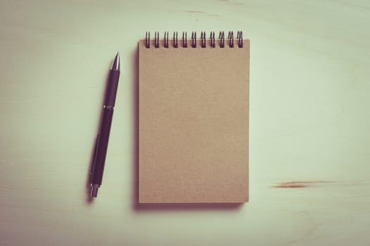 Closed notebook with blank area on front cover on wood table with vintage filter effect