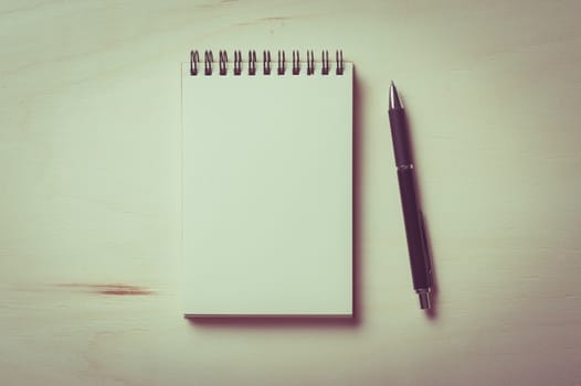 Opened notebook with blank area for text or message and pen on wood table with vintage filter effect