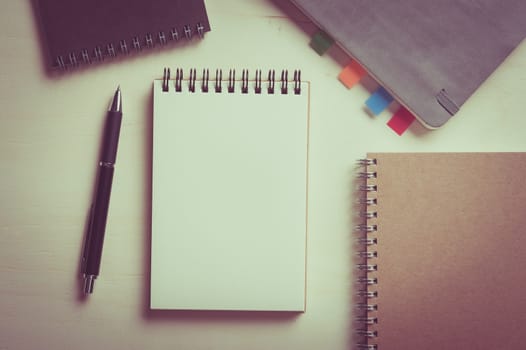 Opened notebook with blank area for text or message, grey, blank, and brown closed notebook on wood table with vintage filter effect