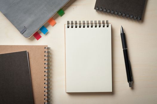 Opened notebook with blank area for text or message, grey, blank, and brown closed notebook on wood table