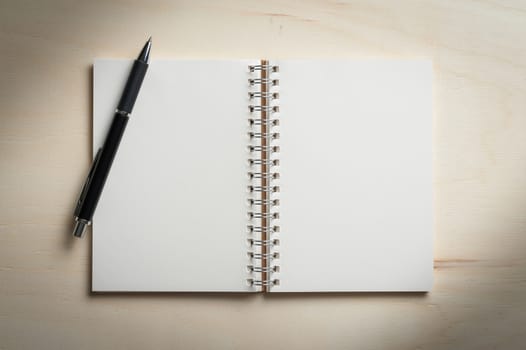 Opened notebook with blank area for text or message and pen on wood table with low key scene