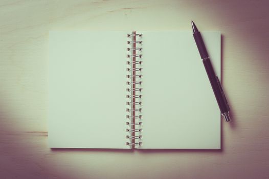 Opened notebook with blank area for text or message and pen on wood table with vintage filter effect