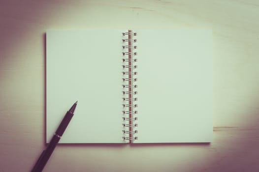 Opened notebook with blank area for text or message and pen on wood table with vintage filter effect
