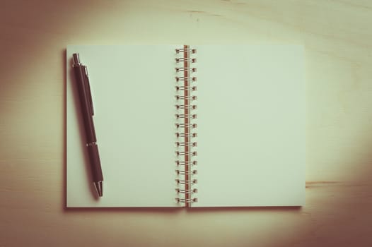 Opened notebook with blank area for text or message and pen on wood table with vintage filter effect