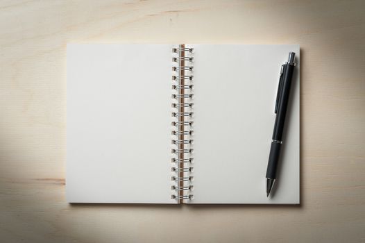 Opened notebook with blank area for text or message and pen on wood table with low key scene