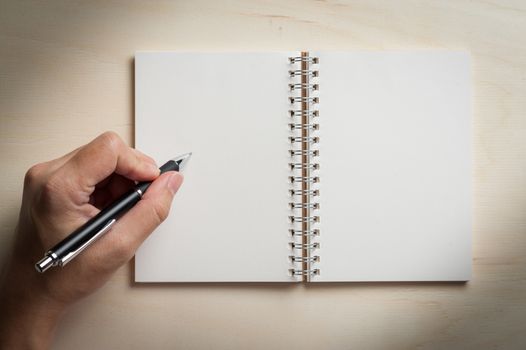 Male left hand writing on opened notebook with blank area for text or message and pen on wood table with low key scene