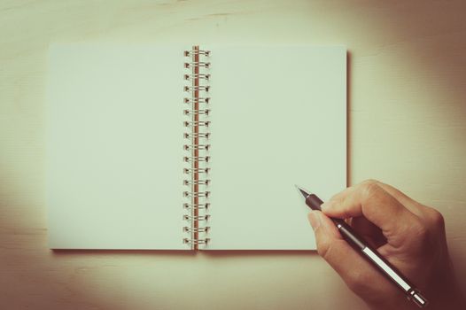 Male right hand writing on opened notebook with blank area for text or message and pen on wood table with vintage filter effect