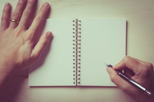 Male right hand writing on opened notebook with blank area for text or message and pen on wood table with vintage filter effect