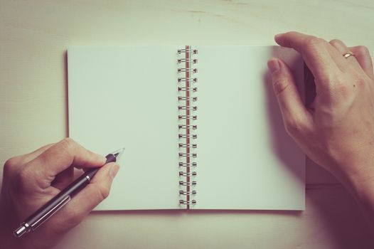 Male left hand writing on opened notebook with blank area for text or message and pen on wood table with vintage filter effect