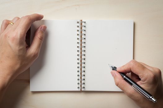 Male right hand writing on opened notebook with blank area for text or message and pen on wood table in morning time
