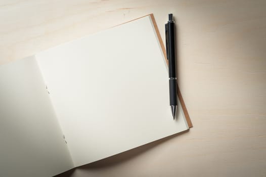 Opened sketch book with blank area for text or message and pen on wood table in morning time with low key scene