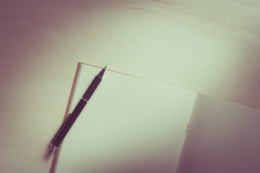 Opened sketch book with blank area for text or message and pen on wood table with vintage filter effect