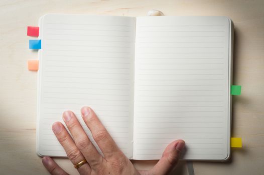 Male left hand touch at opened notebook with blank area for text or message on wood table in morning time with low key scene