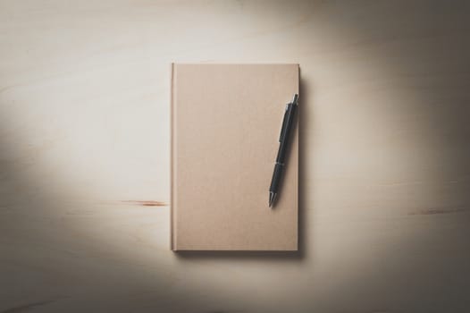 Closed hard cover notebook with blank area on front cover on wood table in morning time with film filter effect