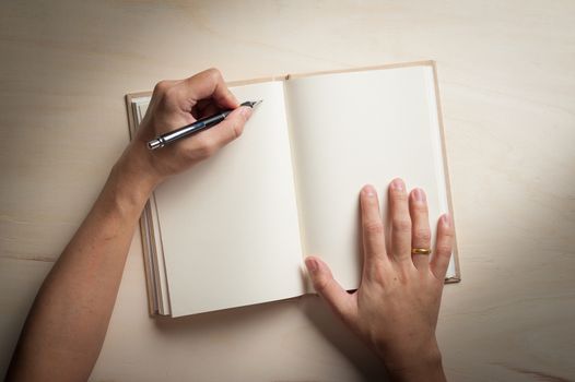 Male left hand writing on opened notebook on wood table in morning time with low key scene