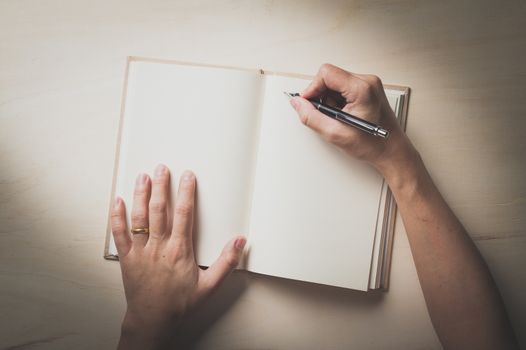 Male right hand writing on opened notebook on wood table in morning time with film filter effect