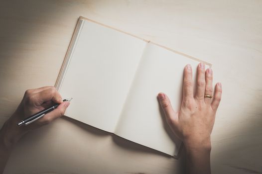 Male left hand writing on opened notebook on wood table with vintage filter effect