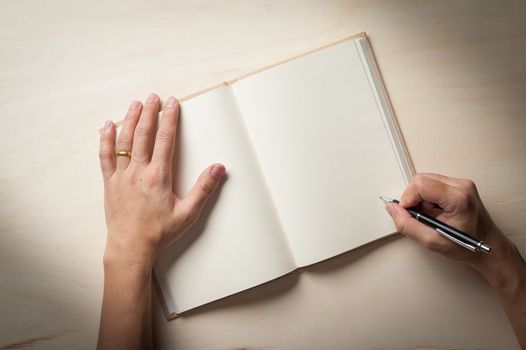 Male right hand writing on opened notebook on wood table in morning time with low key scene