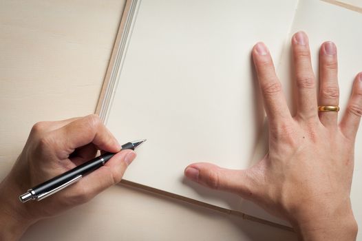 Male left hand writing on opened notebook on wood table in morning time