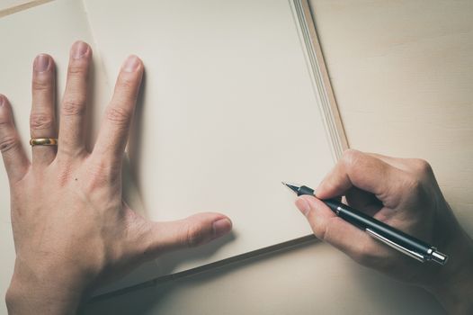 Male right hand writing on opened notebook on wood table in morning time with vintage filter effect