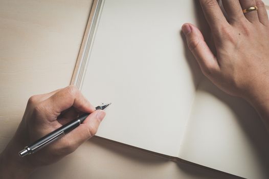 Male left hand writing on opened notebook on wood table with vintage filter effect