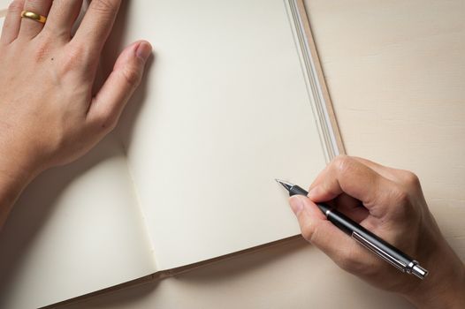 Male right hand writing on opened notebook on wood table in morning time with low key scene