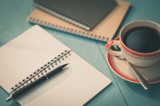 Small notebook and pen beside coffee cup on blue wood table at outdoor area in cafe with morning scene and vintage filter effect