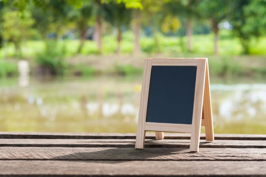 Small A-frame blackboard with blank area for text or message on rustic wood table in morning time
