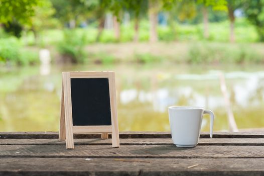 Small A-frame blackboard with blank area for text or message and coffee cup on rustic wood table in morning time