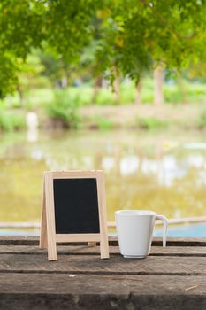 Small A-frame blackboard with blank area for text or message and coffee cup on rustic wood table in morning time