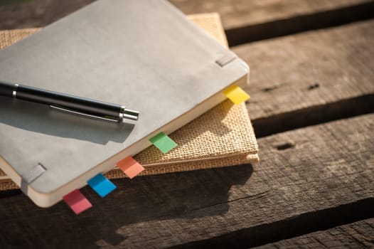 Pen and notebooks on rustic wood table at outdoor area with morning scene in summer time