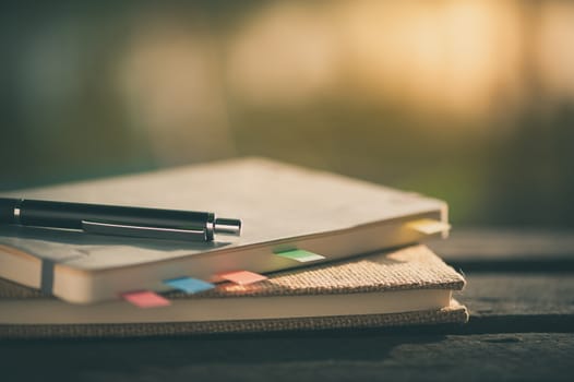 Pen and notebooks on rustic wood table at outdoor area with morning time on summer with vintage filter effect