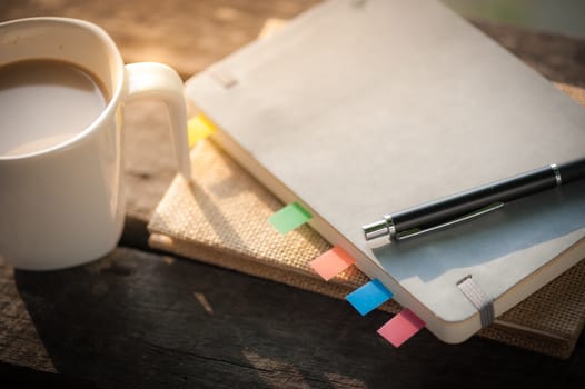 Pen, notebooks, and coffee cup on rustic wood table at outdoor area in morning time