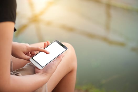 Young woman touching on smartphone blank screen while sitting in park in morning time on weekend