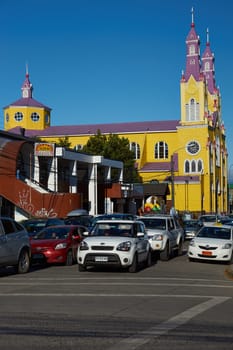 Bright yellow and purple painted Church, San Francisco, on the edge of a busy street filled with traffic in Castro, the capital city of the island of Chiloé in Chile.