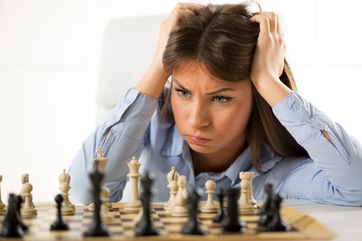 Young beautiful businesswoman devises Business strategy. She sitting above the chessboard with figures and thinking.