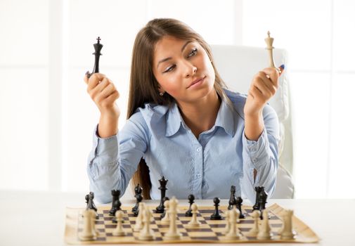 Young beautiful businesswoman devises Business strategy. She sitting above the chessboard with figures and thinking.