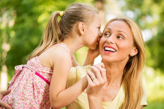 Cute little girl whispering with her mother in the park