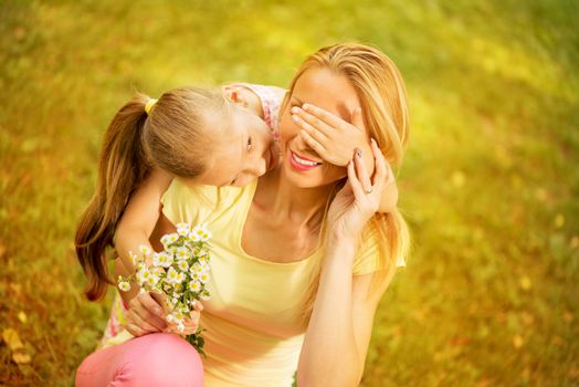 Cute little girl embraced her mother. She is wants surprise with bouquet flowers