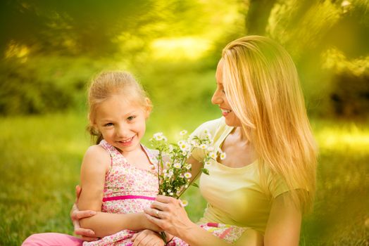 Cute little girl and her mother with bouquet flowers in the park