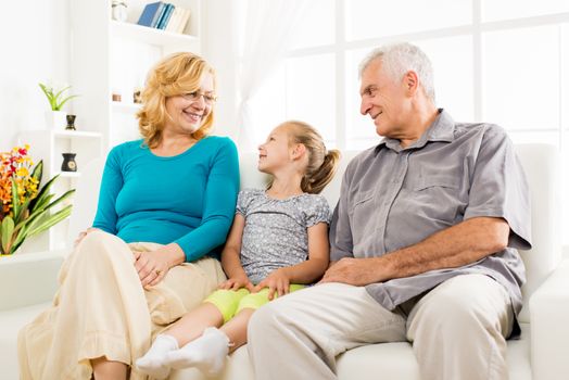 Grandparents with little girl sitting at home and enjoying