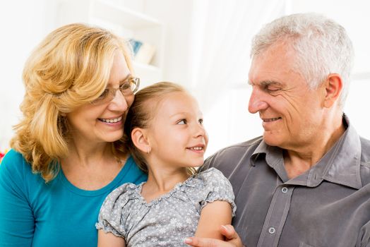 Grandparents with little girl sitting at home and enjoying