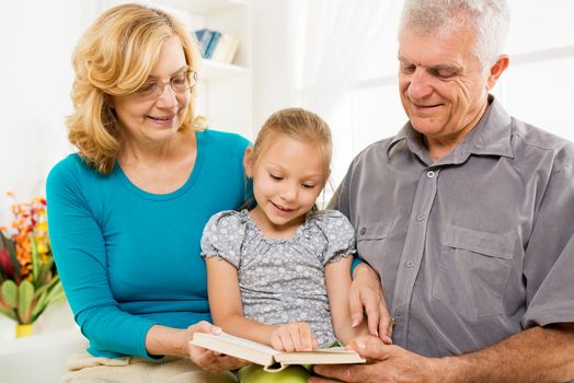 Grandparents with little girl reading book at home